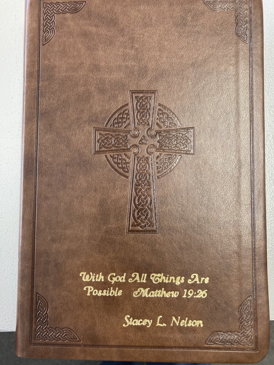 Brown Bible with a gold-foil personal message and name below a decorative cross