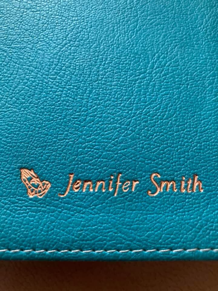 Gold name imprint and praying-hands symbol on a teal Bible