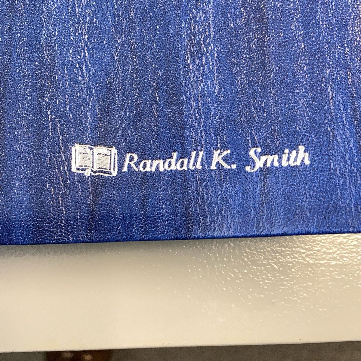 Silver-colored name imprint with an open-Bible symbol on a blue cover